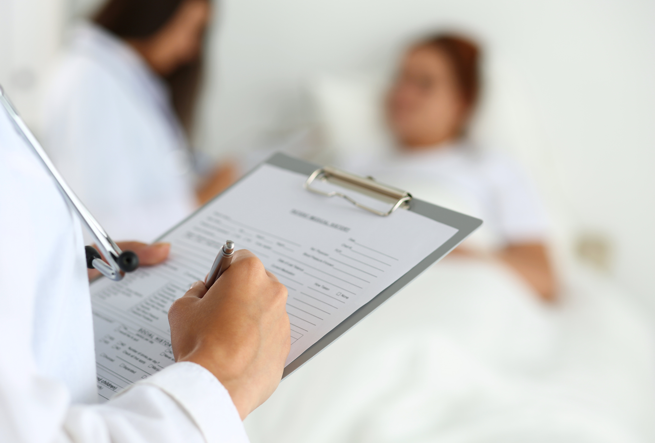 Female Doctor reading patients chart in front of patient in bed